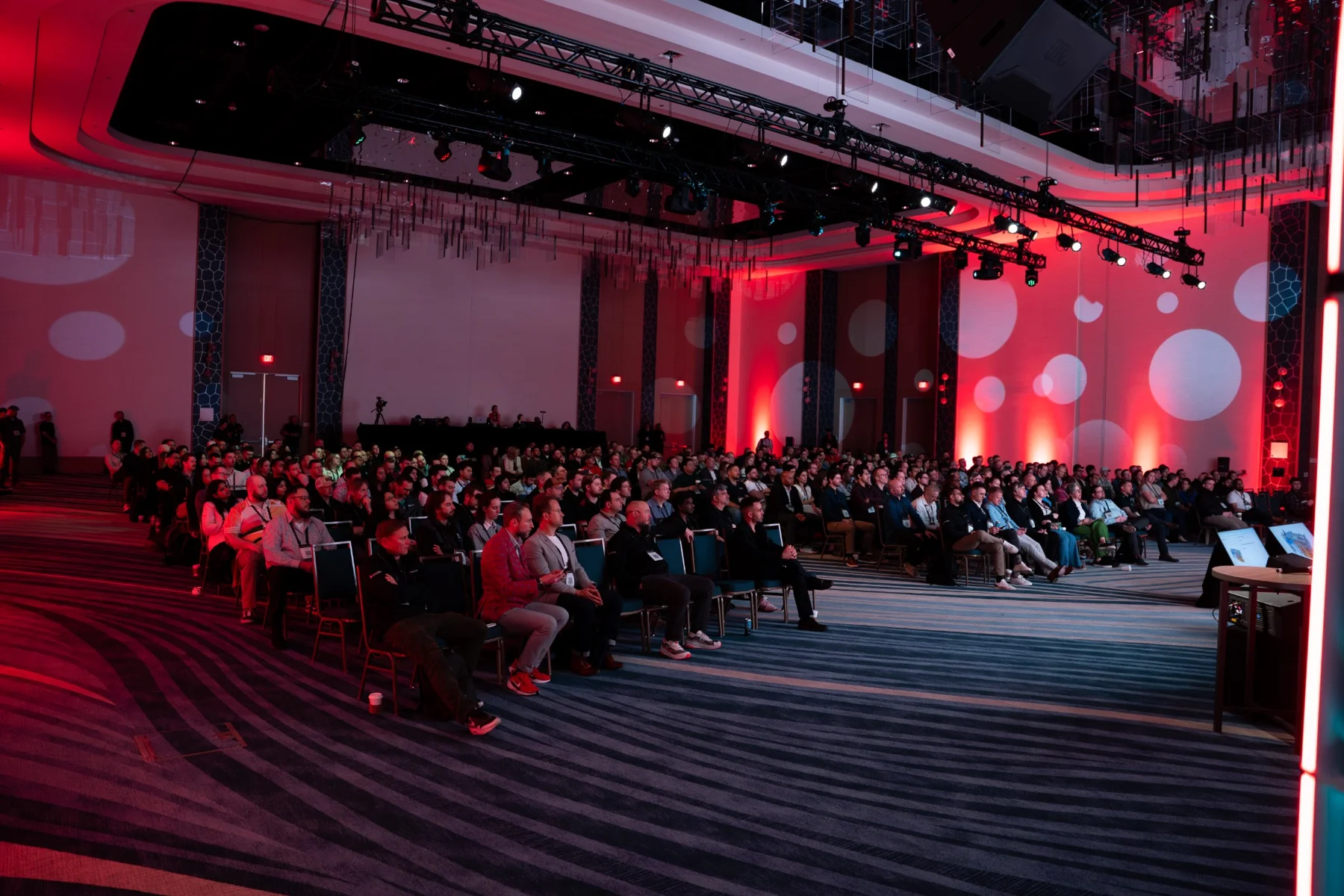 Wide view of a full conference audience under red stage lighting